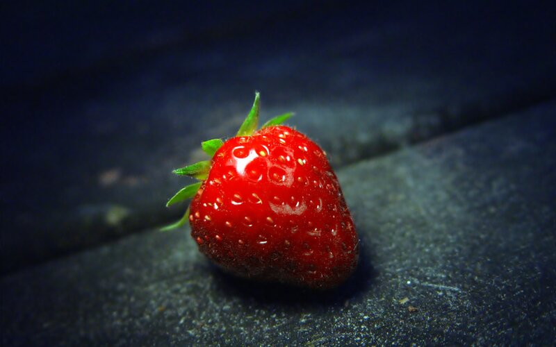 A single strawberry on a dark surface