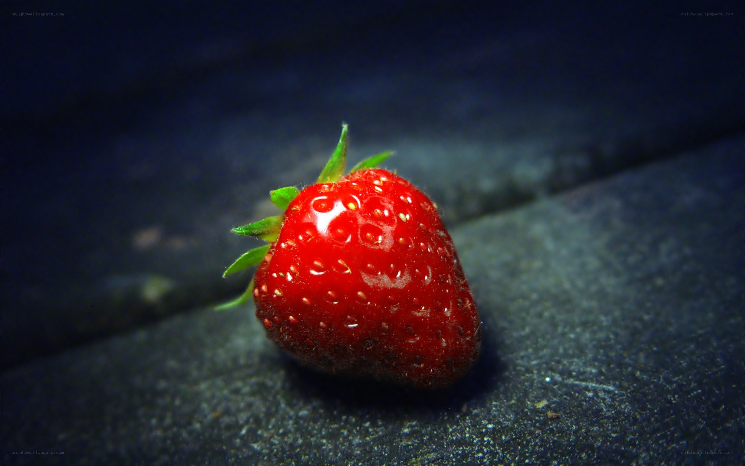 A single strawberry on a dark surface