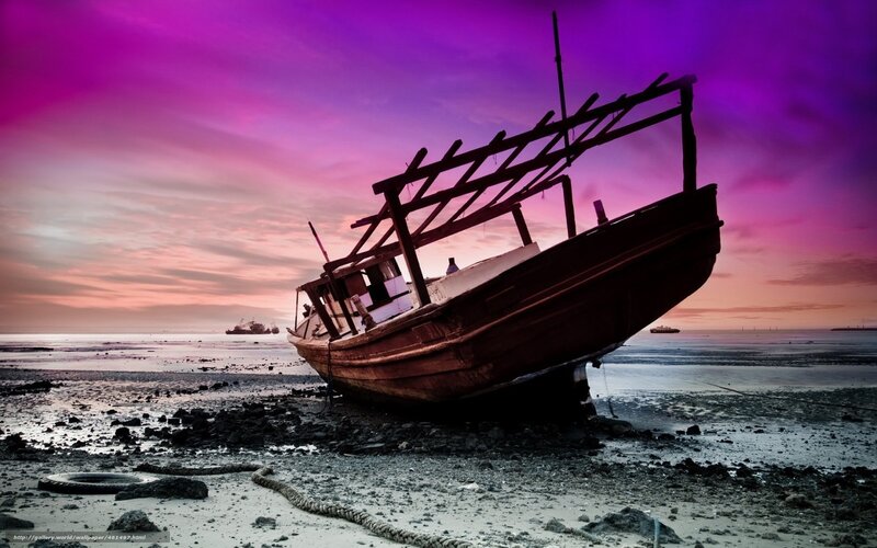 Abandoned boat on beach at sunset
