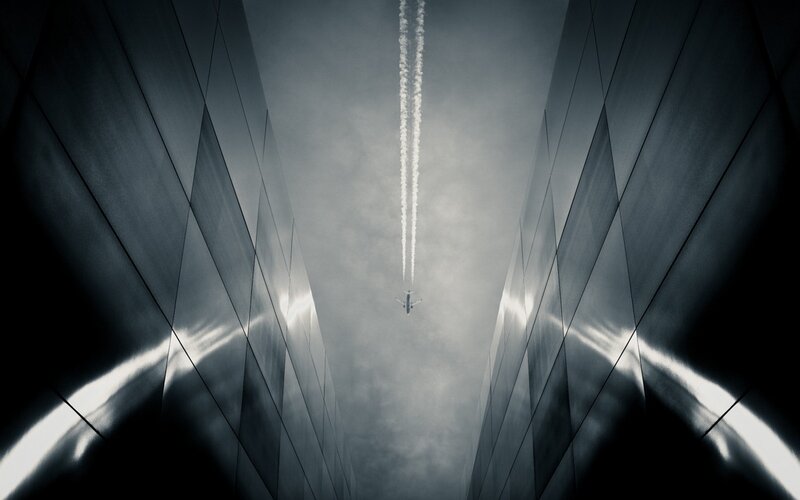 Airplane Flying Between Buildings — Gray