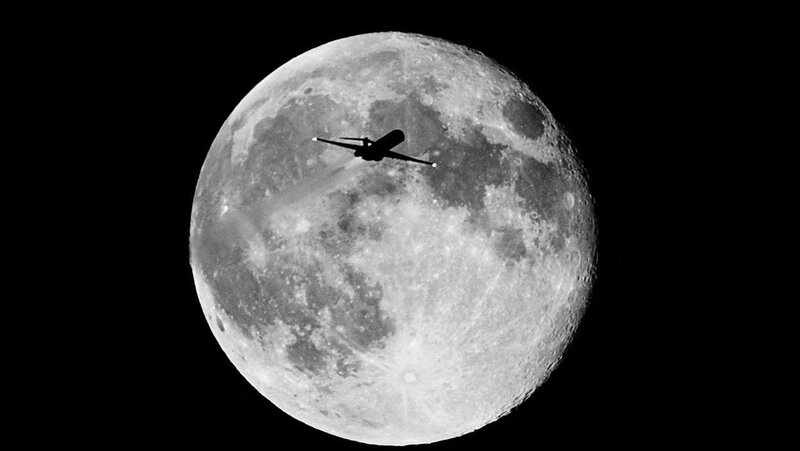 Airplane flying in front of the moon