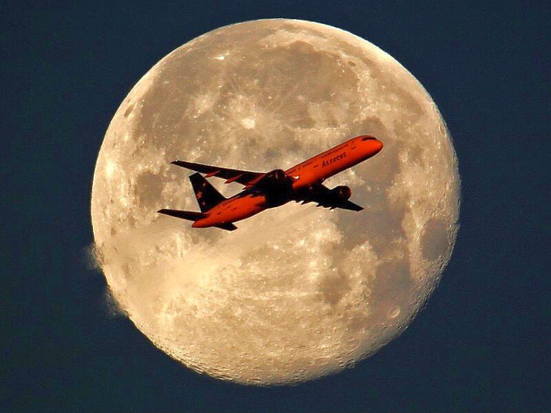 Airplane flying in front of the moon