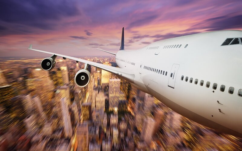 Airplane Flying over City — White