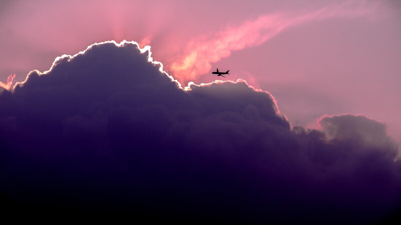 Airplane flying over clouds at sunset