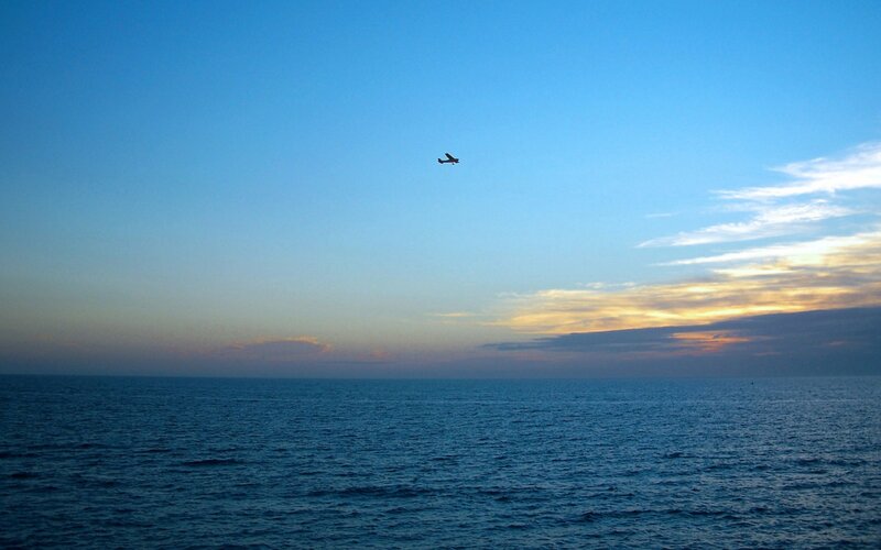 Airplane over the ocean at sunset
