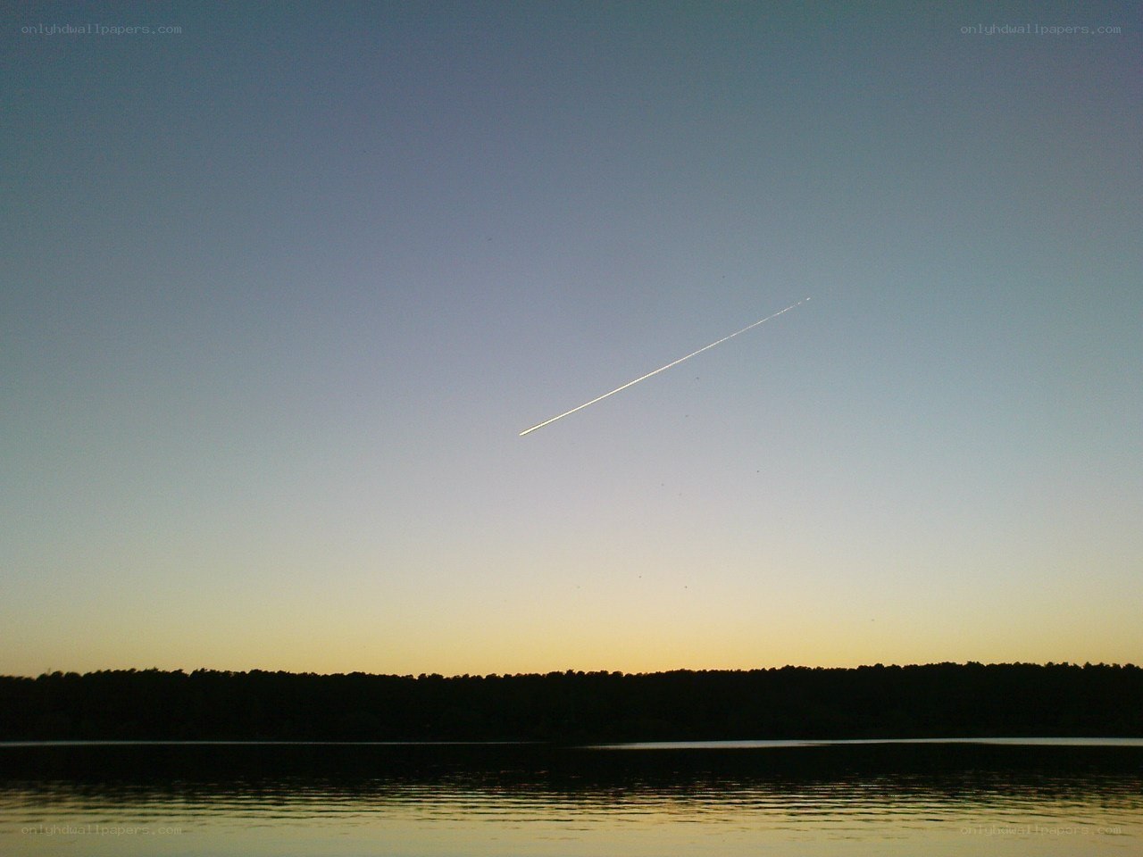 airplane trail over lake at dusk
