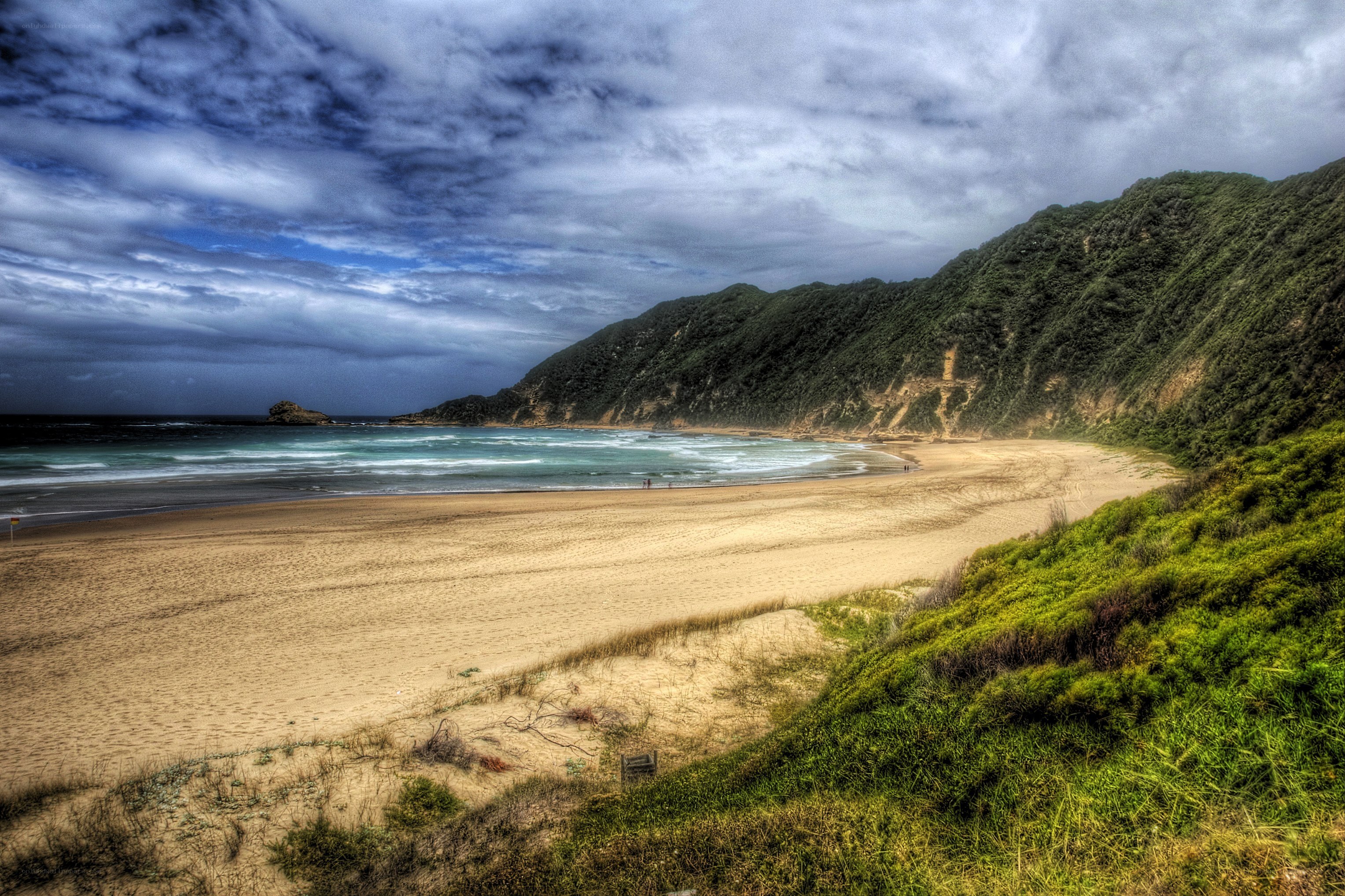 Beach with green hills and cloudy sky