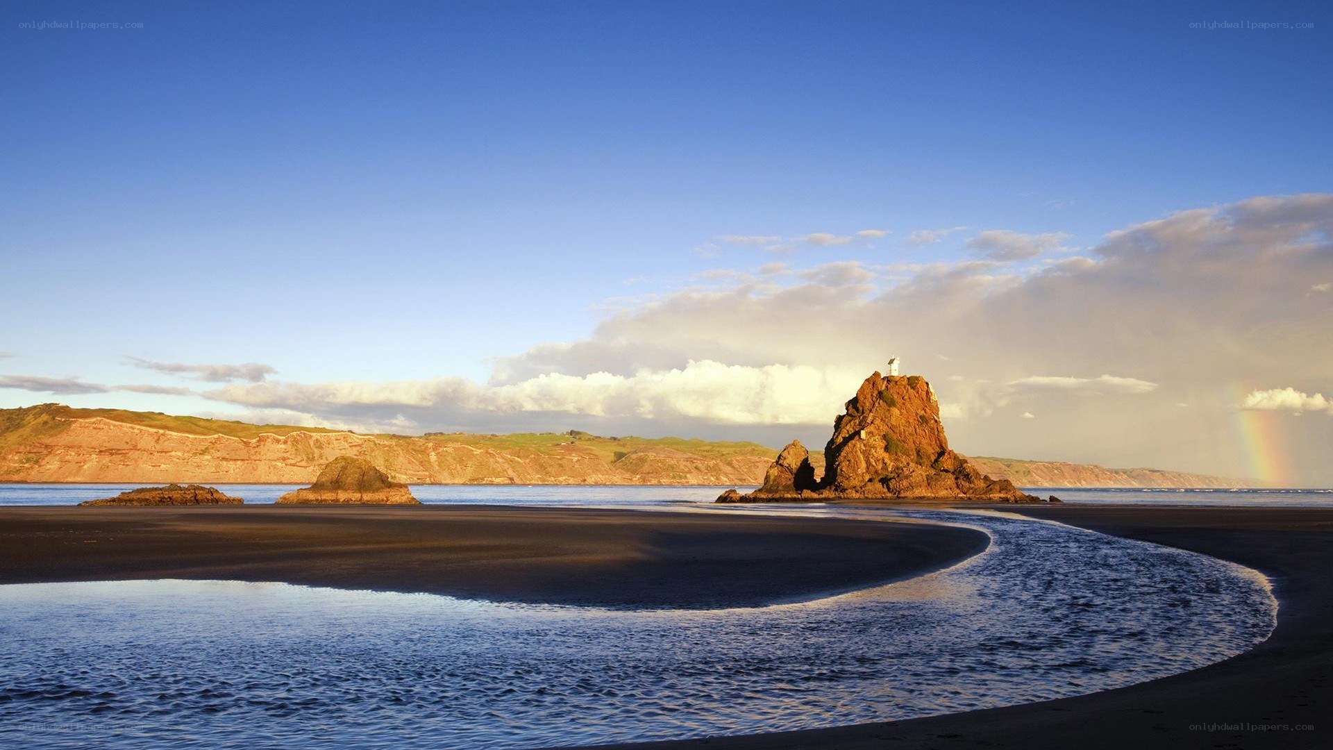beach with rock formation and rainbow