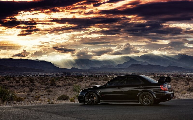 Black car on desert road at sunset