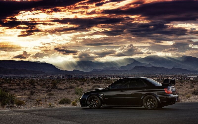 Black car on desert road at sunset