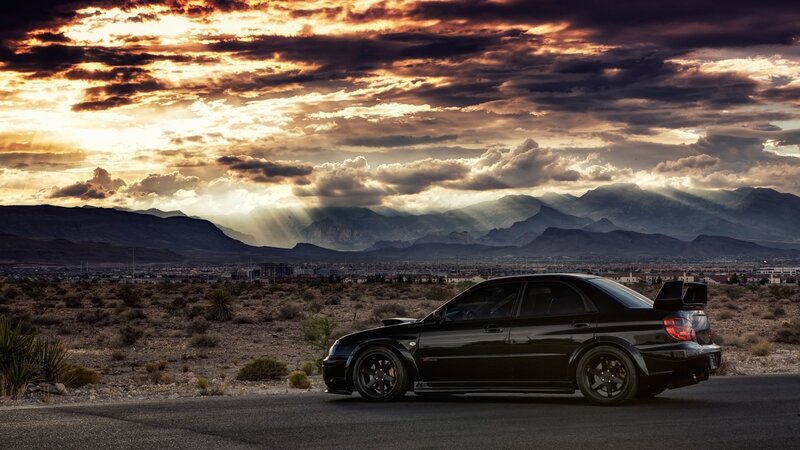 Black car on desert road at sunset