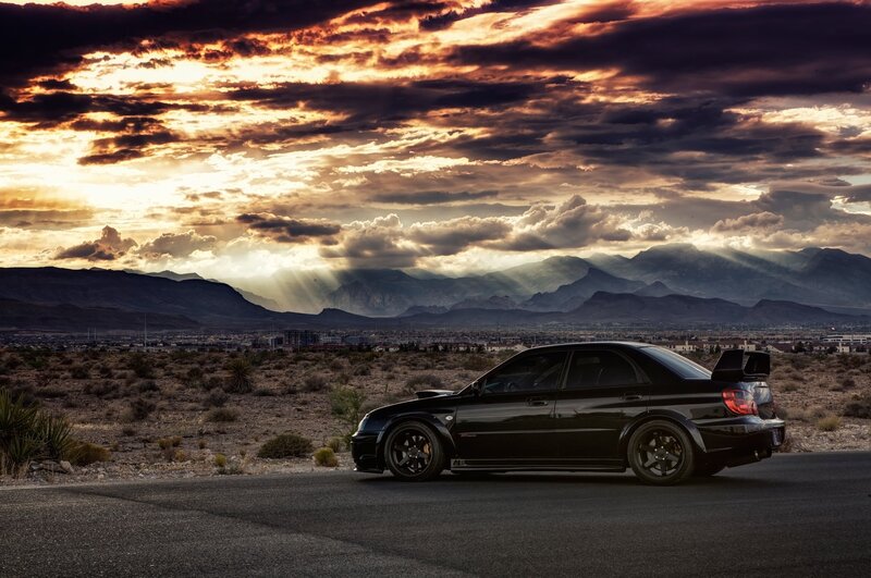 Black car on desert road at sunset