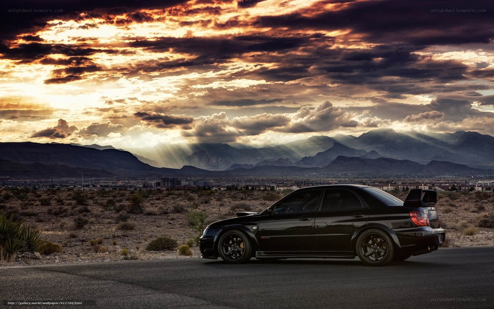 Black car on desert road at sunset