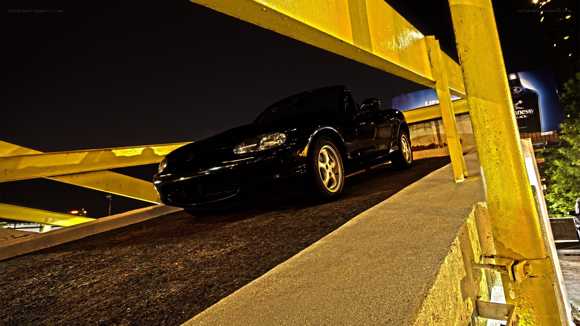Black car under yellow bridge at night