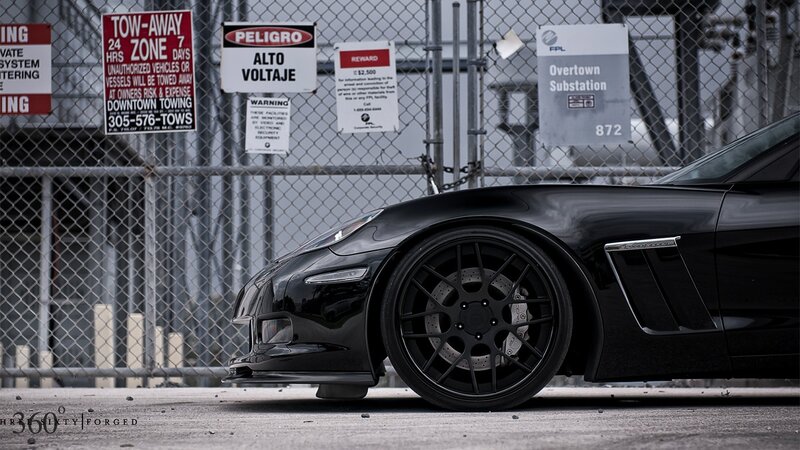 Black Corvette in front of a fence