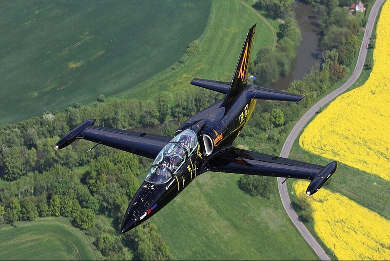 Black jet flying over green fields