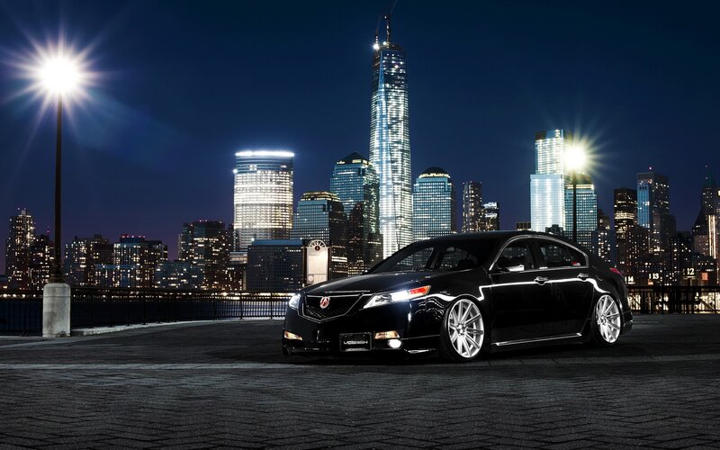 Black sedan at night with city skyline