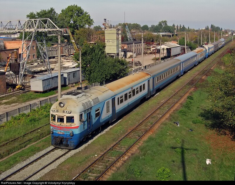 Blue and White Train — Calm, Afternoon, Photograph, Train Tracks, Industrial Buildings