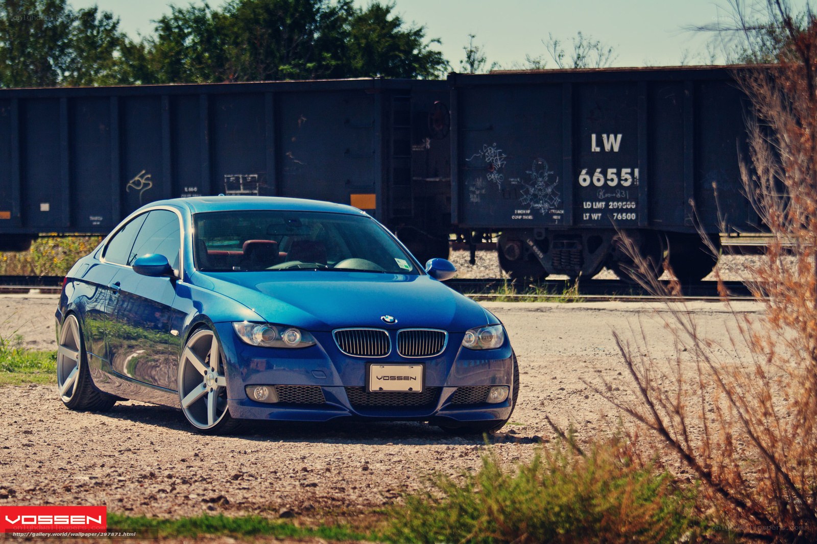 Blue BMW on gravel near train