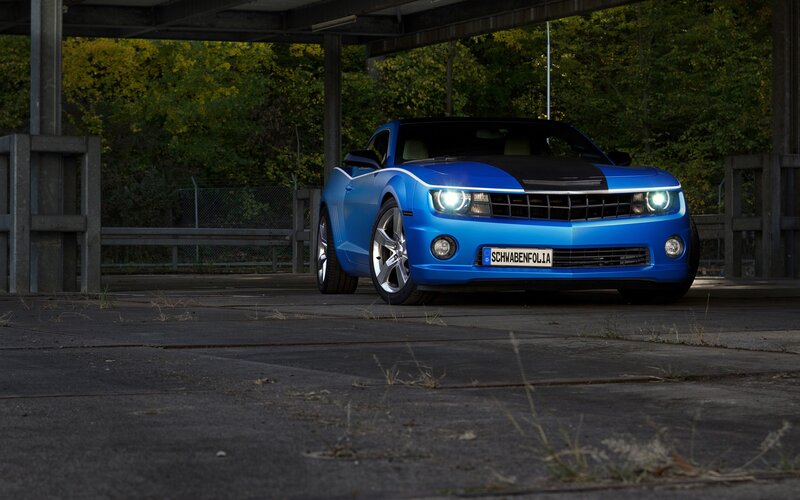 Blue Camaro under a bridge