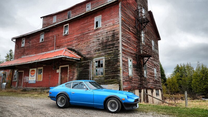 Blue car in front of old red barn