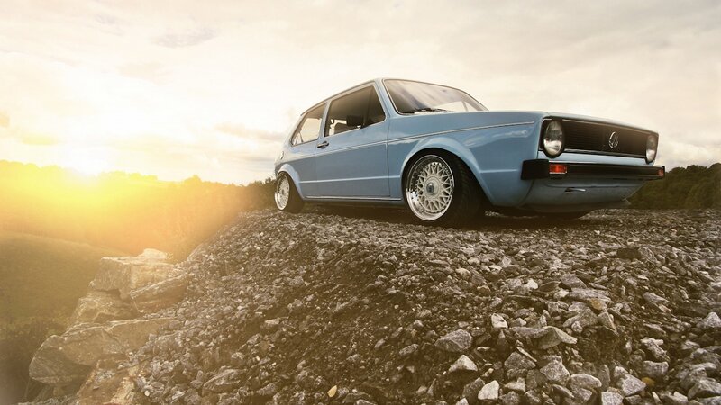 Blue car on rocky hill at sunset