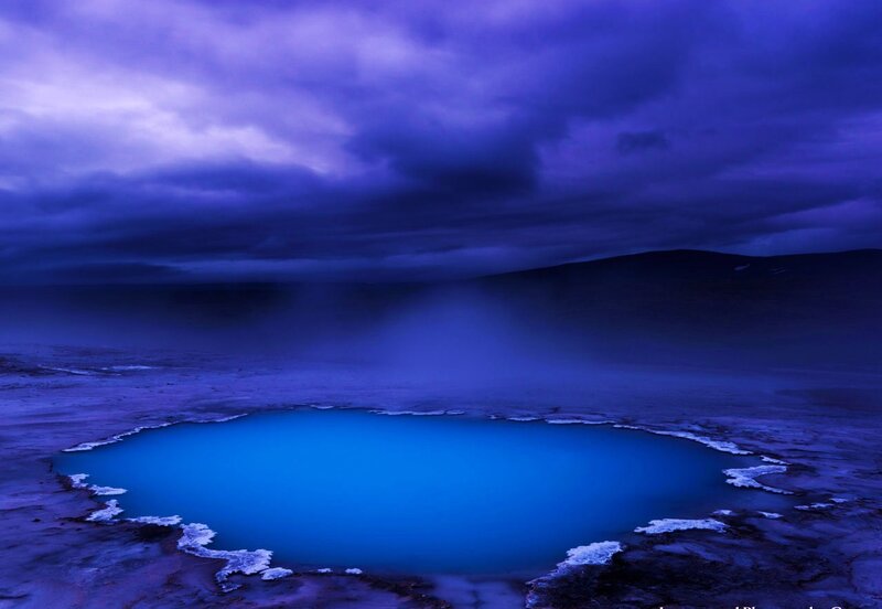 Blue geothermal pool under stormy sky