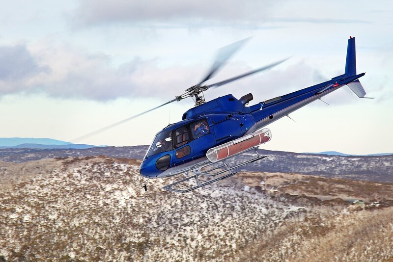 Blue helicopter flying over snowy hills