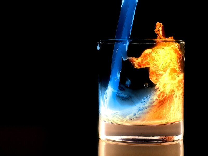 Blue liquid pouring into glass with fire
