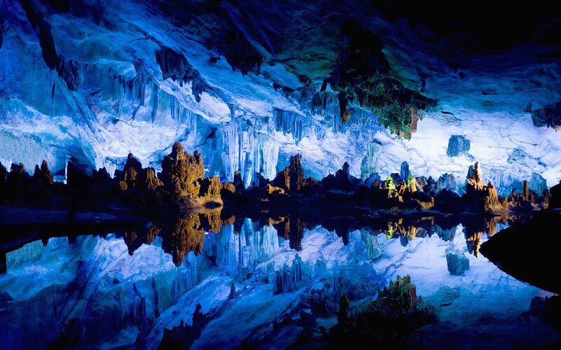 Blue-lit cave with stalactites and stalagmites