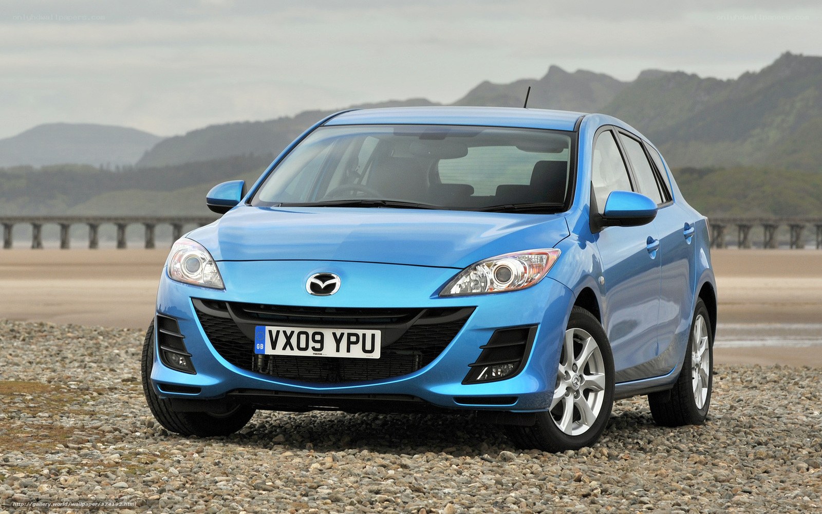 Blue Mazda 3 on a pebble beach