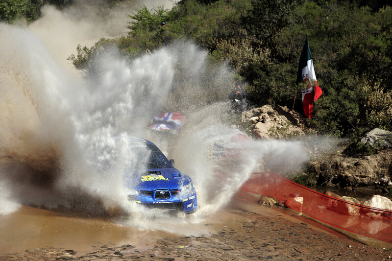 Blue rally car splashing through water