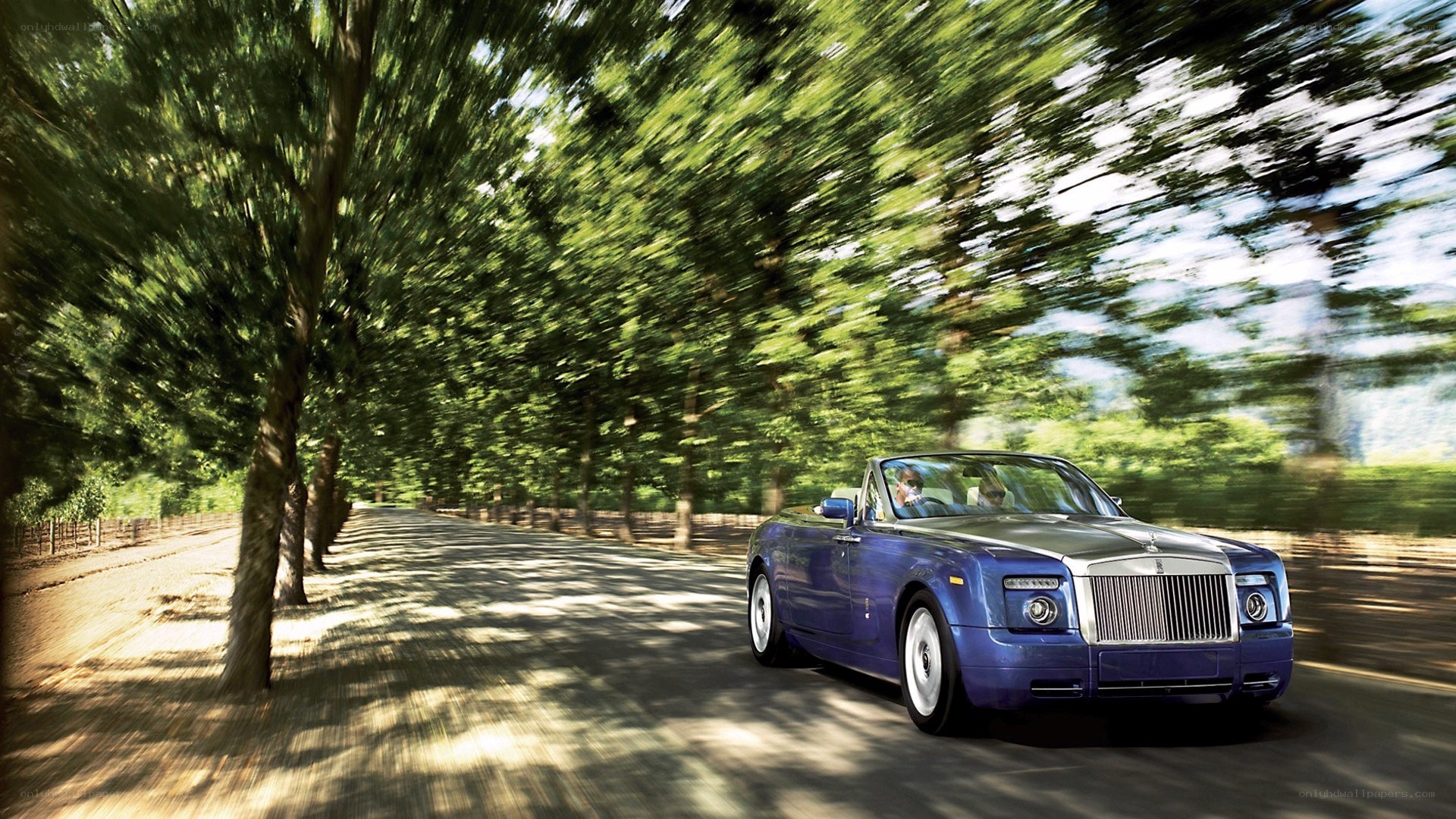 Blue Rolls-Royce convertible on a tree-lined road