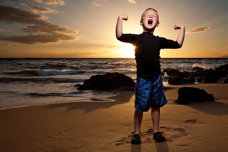 Boy flexing on beach at sunset