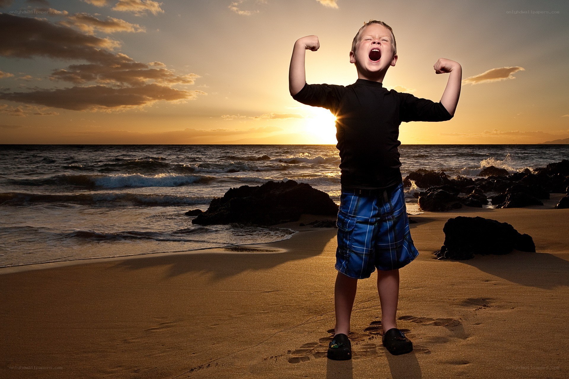 Boy flexing on beach at sunset