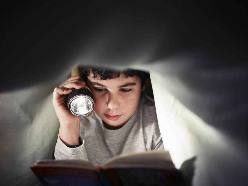 boy reading under blanket