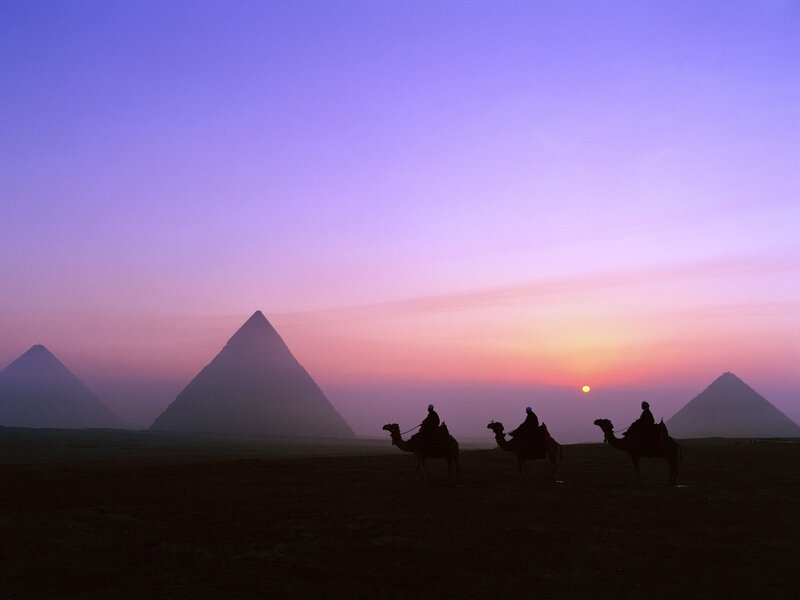 Camel riders at sunset near pyramids