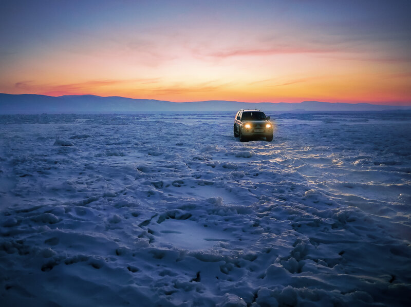 Car on frozen lake at sunset