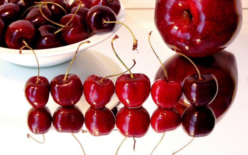 Cherries and apple on reflective surface
