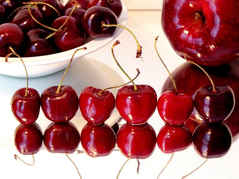 Cherries and apples on a reflective surface