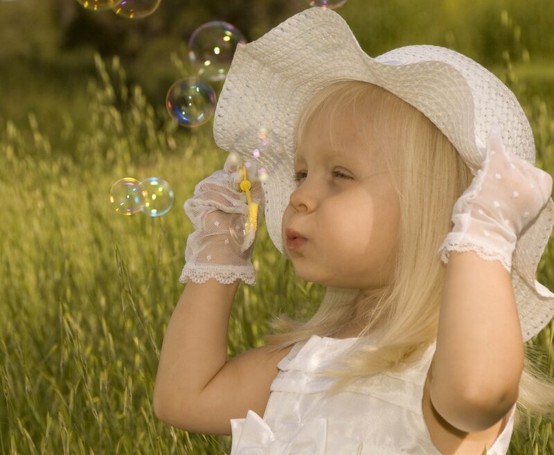 child blowing bubbles in field