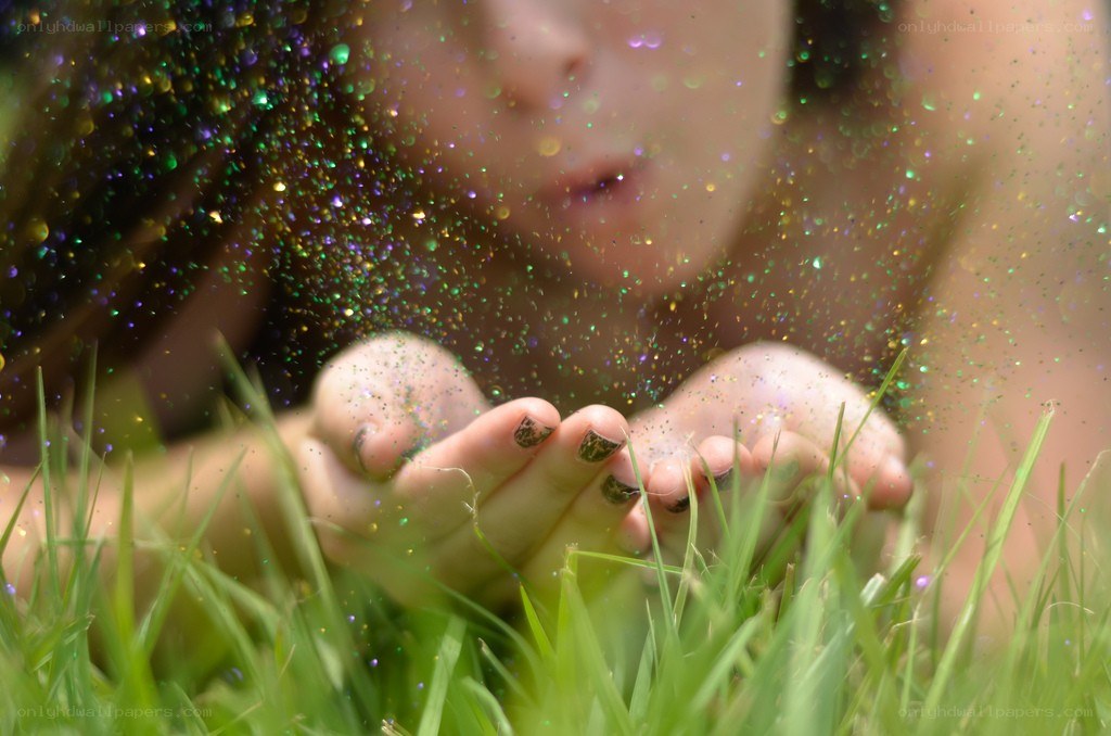 child blowing glitter in grass