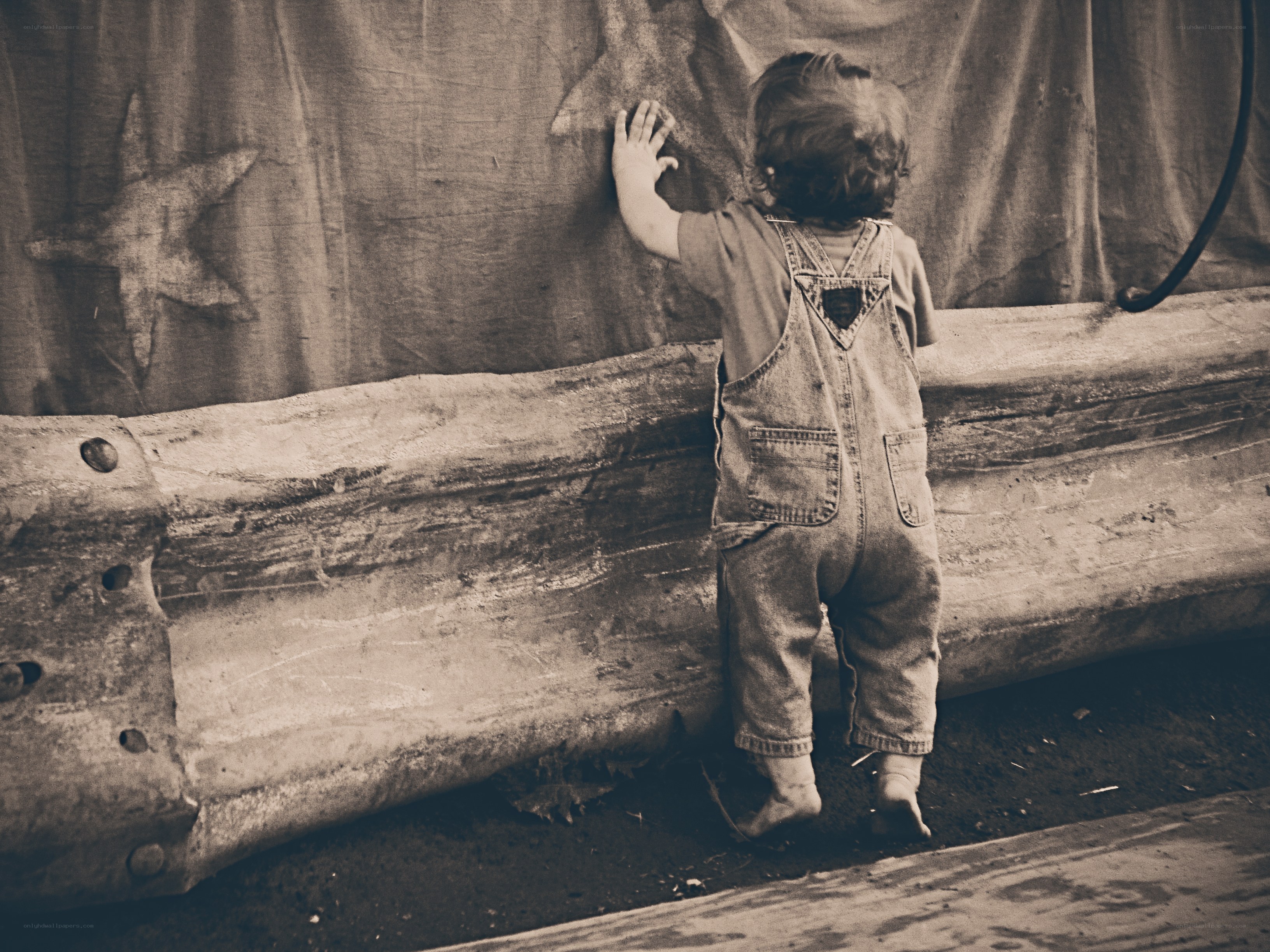 child in overalls touching wall
