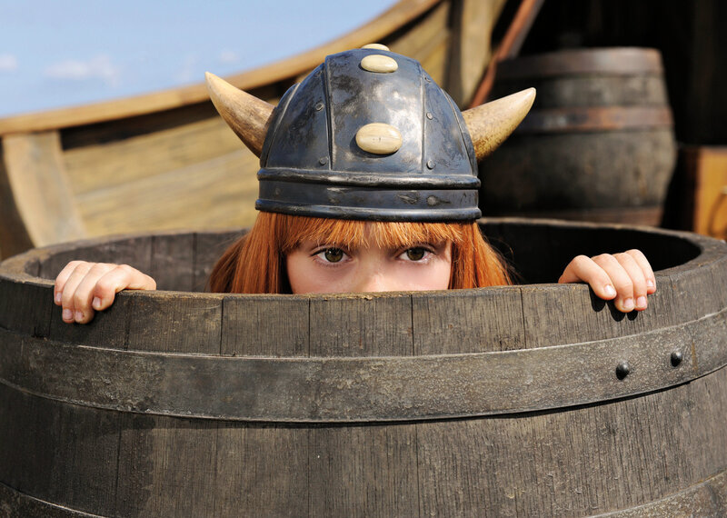 child in viking helmet peeking from barrel