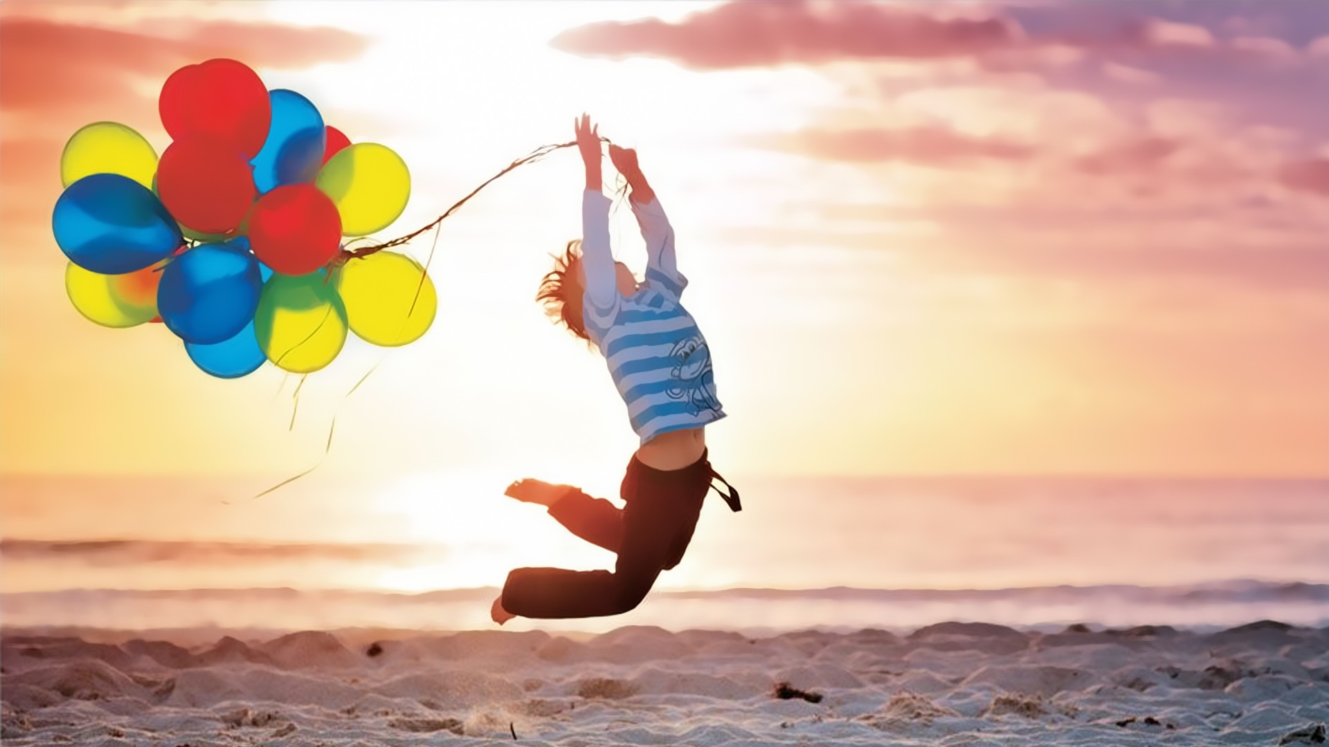 Child jumping with balloons at sunset