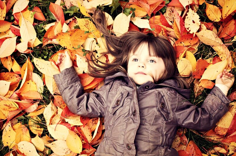 child lying in autumn leaves