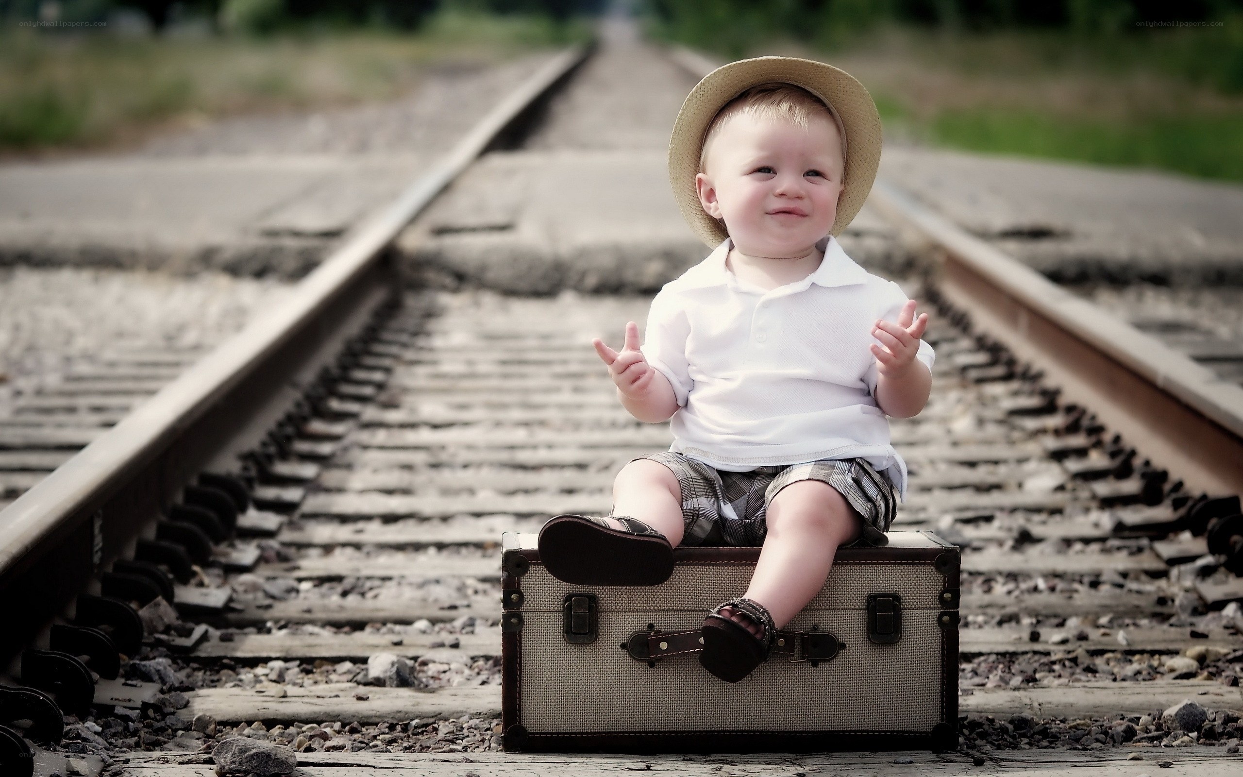 child on suitcase by train tracks