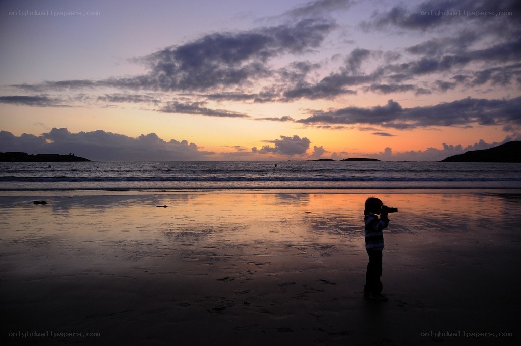 Child photographing sunset on beach