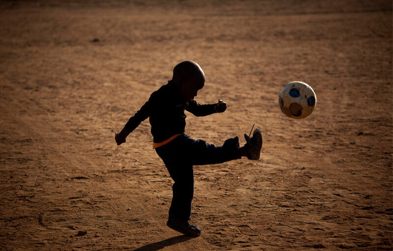 Child playing soccer on dirt field