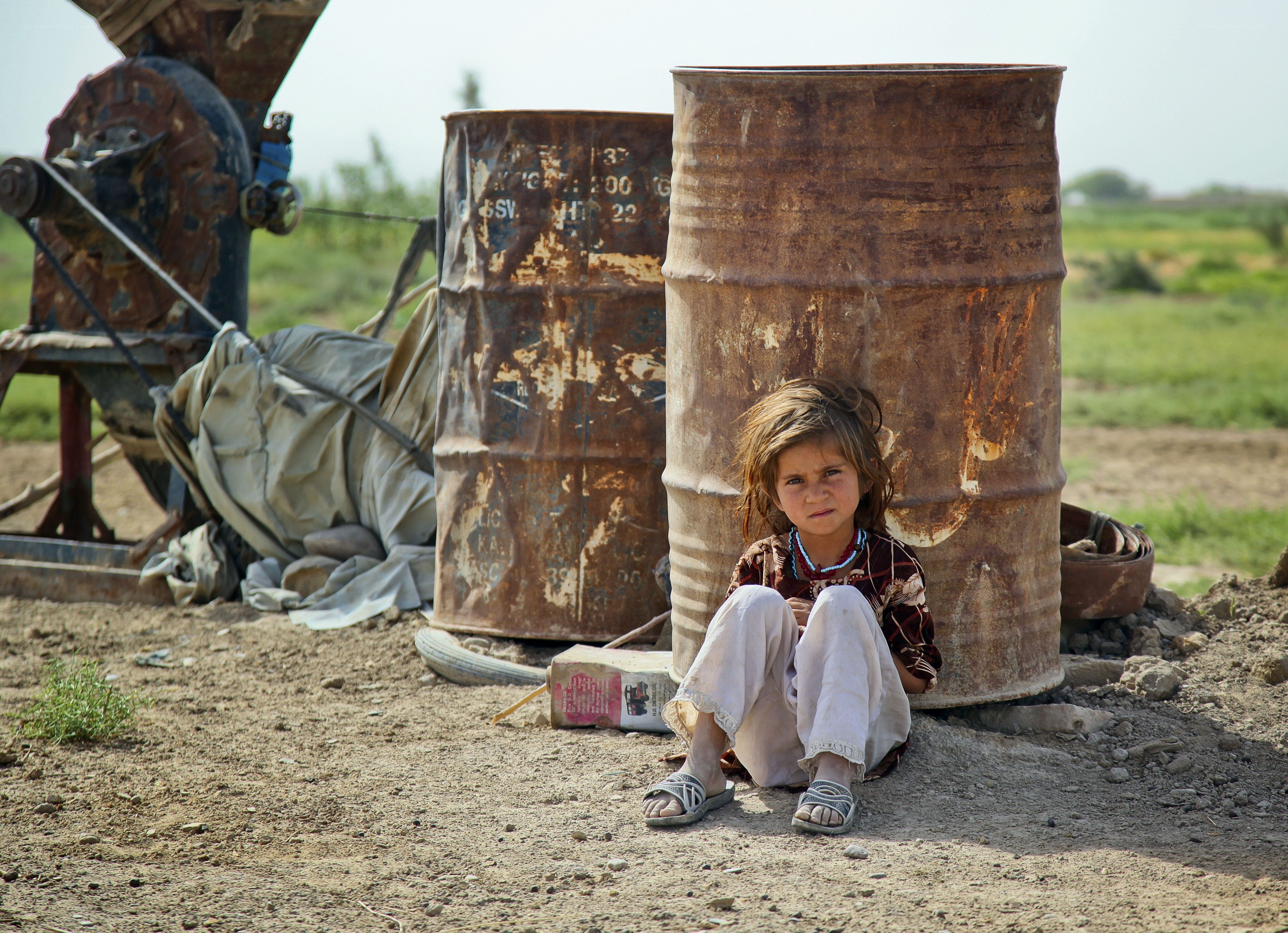 Child sitting by rusted barrels